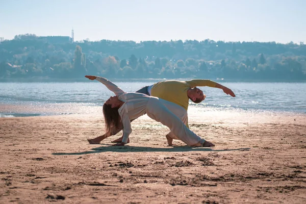 Couple doing yoga, back bend asana, on the beach