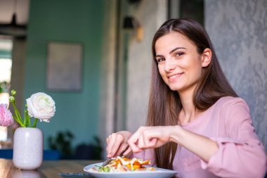 Smiling young woman looking at camera while taking her lunch 