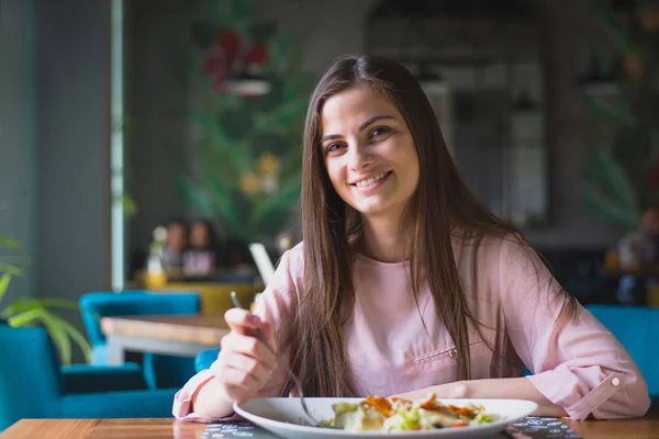 Happy young woman smiles at camera while having lunch