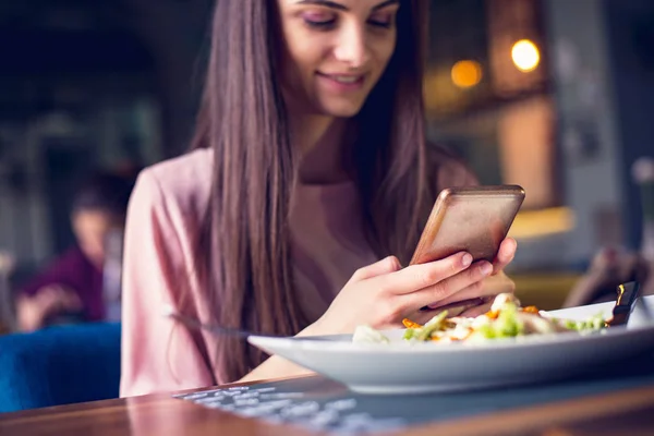 Young teenage girl checking her phone while having lunch — Stockfoto