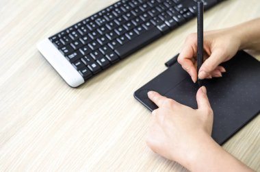 Grafik tabletinde düğme kullanılıyor, sol parmakla düğmeye basılıyor ve sağ elle elektronik kalemle çiziliyor.  