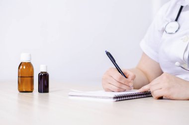 Doktor reçeteli reçete yazıyor. Yakın çekim. İlaç şişeleri masanın üstünde.. 