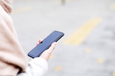 Sokakta elinde siyah cep telefonu olan pembe şallı bir kadın. Boşluğu kopyala. 