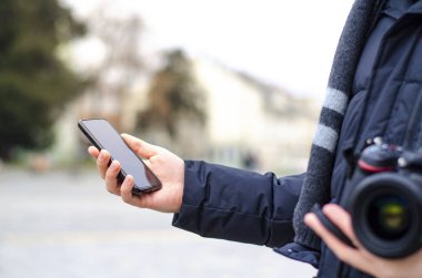 Erkek gezgin telefonunu kontrol ediyor ve elinde fotoğraf makinesi tutuyor. Kış mevsiminde, sokak fotoğrafçısı..