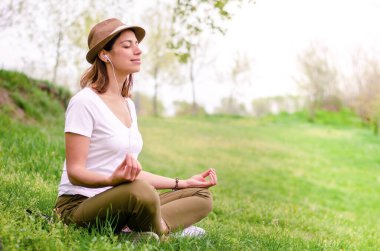 Genç ve güzel bir kadın, müzik dinlerken, doğada meditasyon yapıyor.