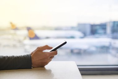 Uçağı beklerken havaalanı terminalinde cep telefonu kullanmak. Cihazı tutan bir kadının yakın çekimi, arka plandaki uçakların görüntüsü.. 