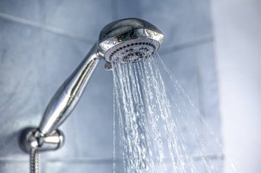 Gümüş bir duş başlığının banyoya su sıçratması.
