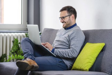 Dizüstü bilgisayar tutan ve evdeki kanepede çalışırken daktilo yazan mutlu bir serbest yazar. 