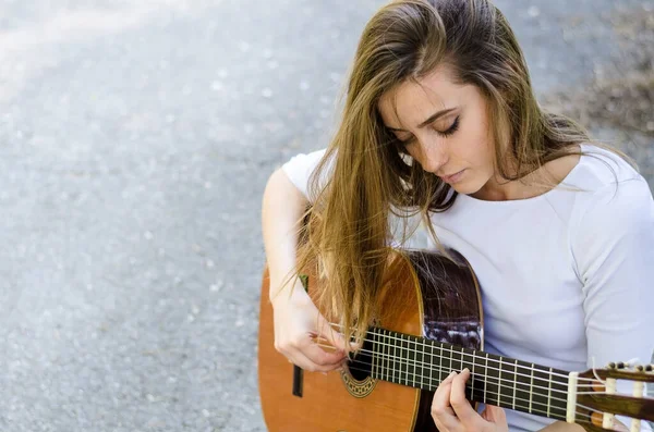 Dışarıda akustik gitar çalan uzun saçlı genç bir kız. Boşluğu kopyala.