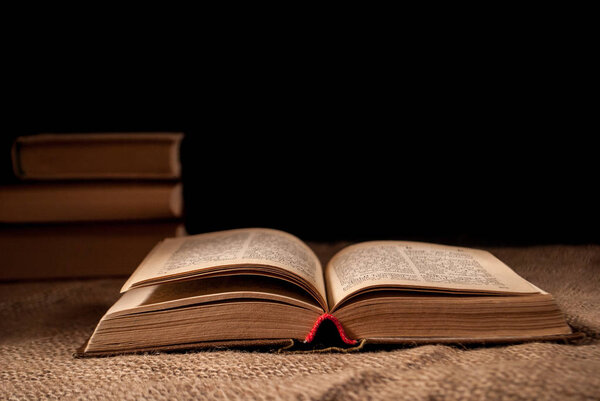 Unfolded book on the surface on a dark background and a pile of books in the background