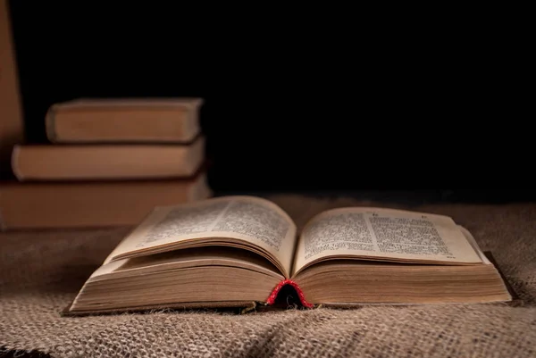 unfolded book on the surface on a dark background and a pile of books in the background