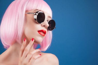 renkli peruğu ve mavi arka plan karşı gümüş güneş gözlüğü giyen güzel kadın