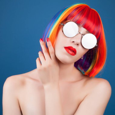renkli peruğu ve mavi arka plan karşı gümüş güneş gözlüğü giyen güzel kadın
