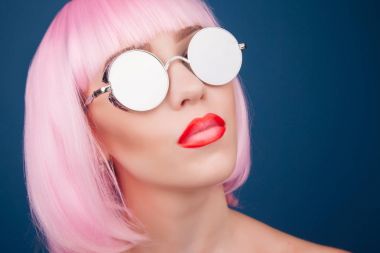 renkli peruğu ve mavi arka plan karşı gümüş güneş gözlüğü giyen güzel genç kadın