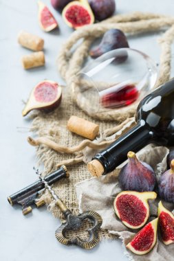 Şişe, tirbuşon, bardak kırmızı şarap, bir tabloda incir