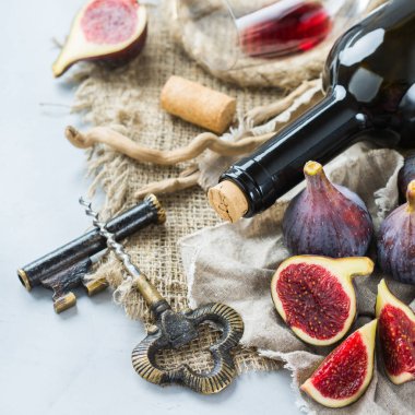 Şişe, tirbuşon, bardak kırmızı şarap, bir tabloda incir