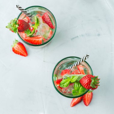 Gıda ve içecek, tatil partisi konsepti. Soğuk taze alkol içecek mojito gözlüklü beyaz rom, soda, kırmızı çilek ve fesleğen yaz günlerinde serinlemek için kokteyl. Üstten görünüm arka plan