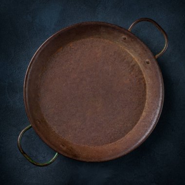 Karanlık bir masanın üzerine boş dökme demir tava.