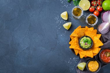 Sarı mısır cipsi, guacamole soslu nachos, kırmızı acı biberli biber sosu ve siyah bir masada tekila ile peynir sosu. Üst görünüm düz kopya alanı arkaplanı 