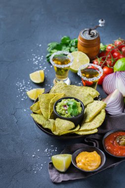 Sarı mısır cipsli Meksika cipsi, kırmızı acı biberli jalapeno sosu ve siyah bir masada tekila ile peynir sosu..