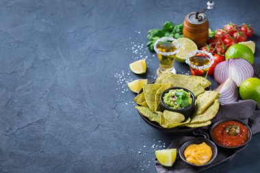 Sarı mısır cipsi, guacamole soslu nachos, kırmızı acı biberli biber sosu ve siyah bir masada tekila ile peynir sosu. Boşluk arkaplanı kopyala 