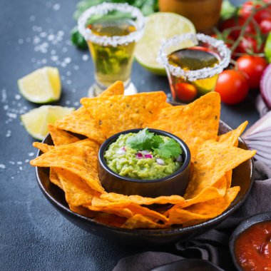 Sarı mısır cipsli Meksika cipsi, kırmızı acı biberli jalapeno sosu ve siyah bir masada tekila ile peynir sosu..