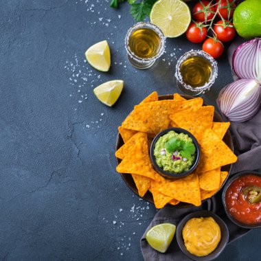 Sarı mısır cipsi, guacamole soslu nachos, kırmızı acı biberli biber sosu ve siyah bir masada tekila ile peynir sosu. Üst görünüm düz arkaplan 