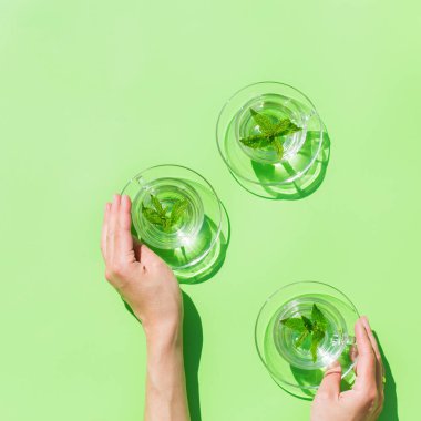 Rahatlama, stres, endişe, kronik yorgunluk, depresyon azaltma ve azaltma konsepti. Kadın ellerinde nane çayı, güneşli, canlı, sert ışık ve açık havada, yeşil arka planda gölgeler.