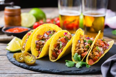 Taco kabuğu, mısır cipsi kıyma, kıyma, guacamole, kırmızı acı biber sosu ve peynir soslu tekila ya da birayla kaplı cips cipsi..