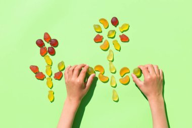 Childs 'ın elleri jöleli meyve şekerlerinden çiçek yapıyor, nane yeşili arkaplanda tatlılar. Çocuk sanatları ve el sanatları, yaratıcı sanat eserleri, diy, kendi kendine eğlence, eğitim, öğrenme konsepti