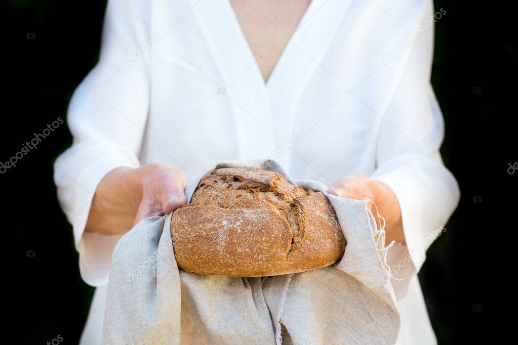 Mature senior woman holding freshly baked loaf of homemade rye bread in her hands