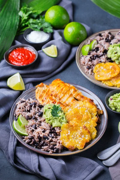 Traditional Central American caribbean cuban colombian food. Rice with black beans, roasted fried chicken breast and tostones, fried green bananas plantains with guacamole sauce