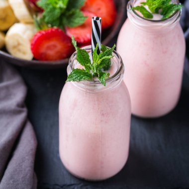 Yiyecek ve içecek, sağlıklı beslenme ve beslenme, yaşam tarzı, vegan, alkalin, vejetaryen konsepti. Modern bir mutfak masasında muzlu ve çilekli pembe smoothie. Boşluk arkaplanı kopyala
