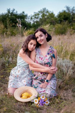 Güzel kız, gülümseyen annesine şefkatle sarılıyor güneşli yaz gününde çimlerin üzerinde oturuyor.