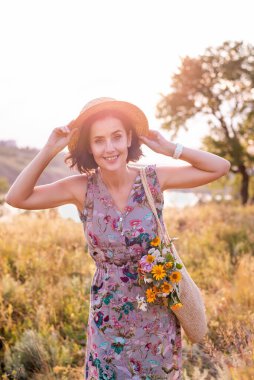 İki eli kafasında hasır şapka tutan bir kadın.