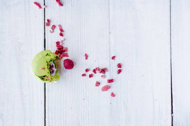 Beyaz ahşap zeminde tatlı renkte makarna kurabiyesi. Kompozisyon ahududu, kırmızı çilek parçalarıyla süslenmiş. Anneler günü için tebrik kartı, poster kartı..