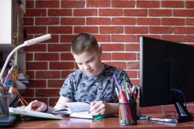 Akıllı bir genç çocuk masada oturuyor, ödev yapıyor ya da sınava hazırlanıyor. Ev ödevi, dizüstü bilgisayarlar, kitaplar, notlar, lambalar. Dijital eğitim kavramı, evde karantina altındayken..
