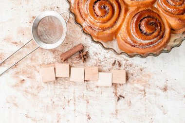 Taze pişmiş tarçınlı rulo ya da tarçınlı büyük cam tabaklara. Tarçın, karanfil, kakao tozu, süzgeç ve altı boş tahta küp retro ahşap arka plan metni. Anlaşıldı.
