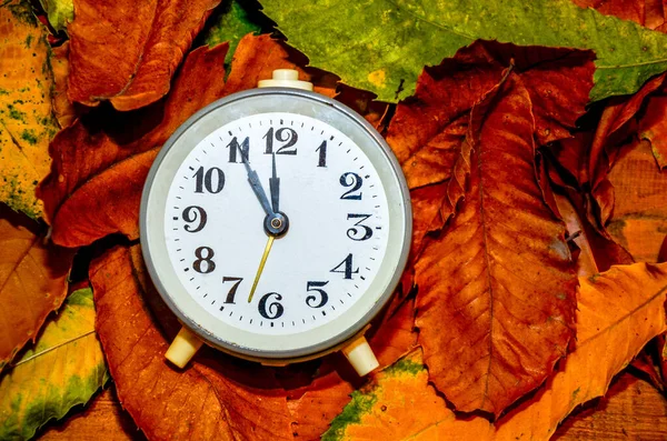Daylight saving time. Retro styled photo. Vintage black alarm clock on autumn leaves. Time change abstract photo. Daylight saving time (DST)