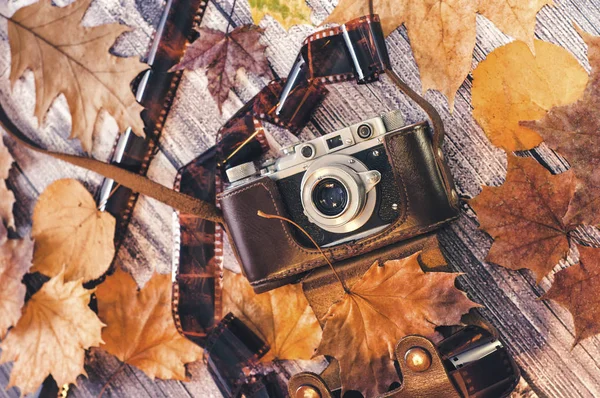 Composición de otoño. Cámara retro, hojas de otoño, damas sobre un fondo de madera y un cojín de hojas de otoño. Película vintage alrededor de la cámara. Nostalgia por el otoño. La vista desde arriba . — Foto de Stock