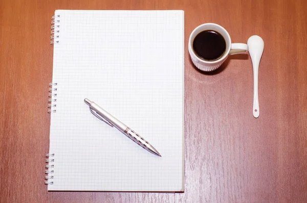 Το σημειωματάριο, στυλό και λευκό φλιτζάνι με τον καφέ στο τραπέζι — Φωτογραφία Αρχείου