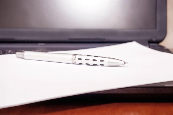 Laptop, hoja blanca de papel y pluma sobre la mesa —  Fotos de Stock