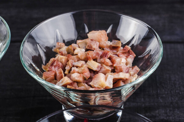 Herring in a transparent deep dish chopped finely cubes on a wooden black background.