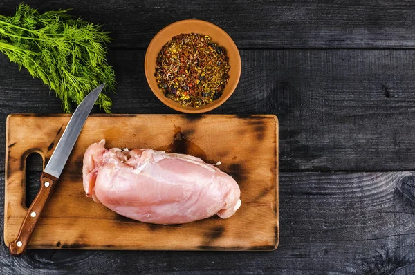 Fresh raw chicken fillet on a cutting board with a knife, spices