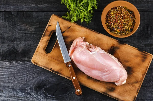 Fresh raw chicken fillet on a cutting board with a knife, spices