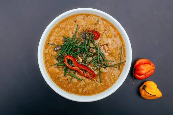 Weiße Schale einer gesunden vegetarischen Erbsensuppe mit Kürbiskernen, Schnittlauch und würzigem Chili. Orange Farbe, schwarzer Hintergrund, dunkle Food-Fotografie — Stockfoto