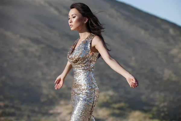 Young fashion asian model in a luxury golden dress posing in a desert