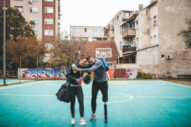 Young man with prosthetic leg enjoying with his friend at basketball court. clipart