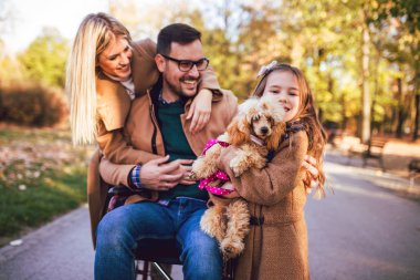 Tekerlekli sandalyedeki engelli baba, kızı ve karısıyla birlikte sonbahar parkında eğleniyor..
