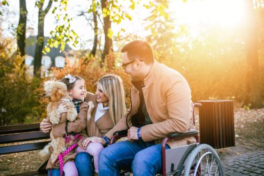 Tekerlekli sandalyedeki engelli baba parkta kızı, karısı ve köpeğiyle eğleniyor..